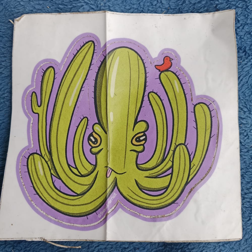 A sticker of a smiling green cactus shaped like an octopus, with a small red bird sitting on one arm, on a purple background, signed ShowerPanther